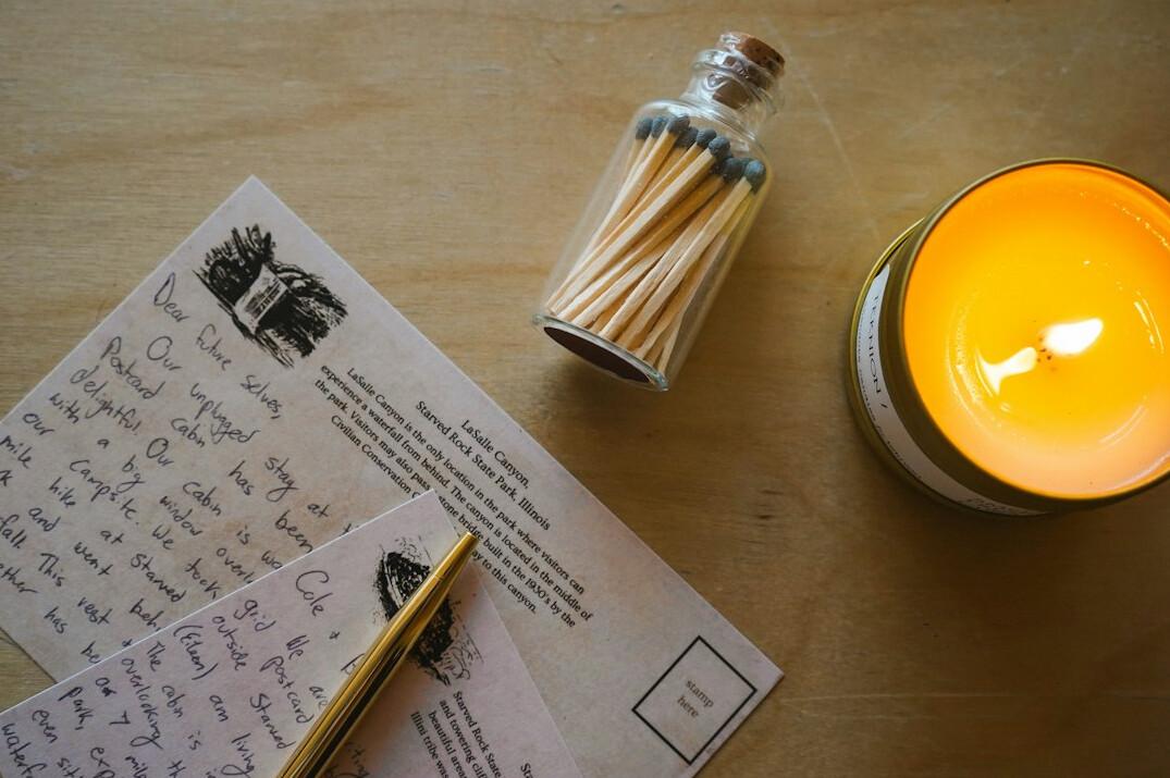 Old wooden writing desk with letters, an ink pen and a lit candle